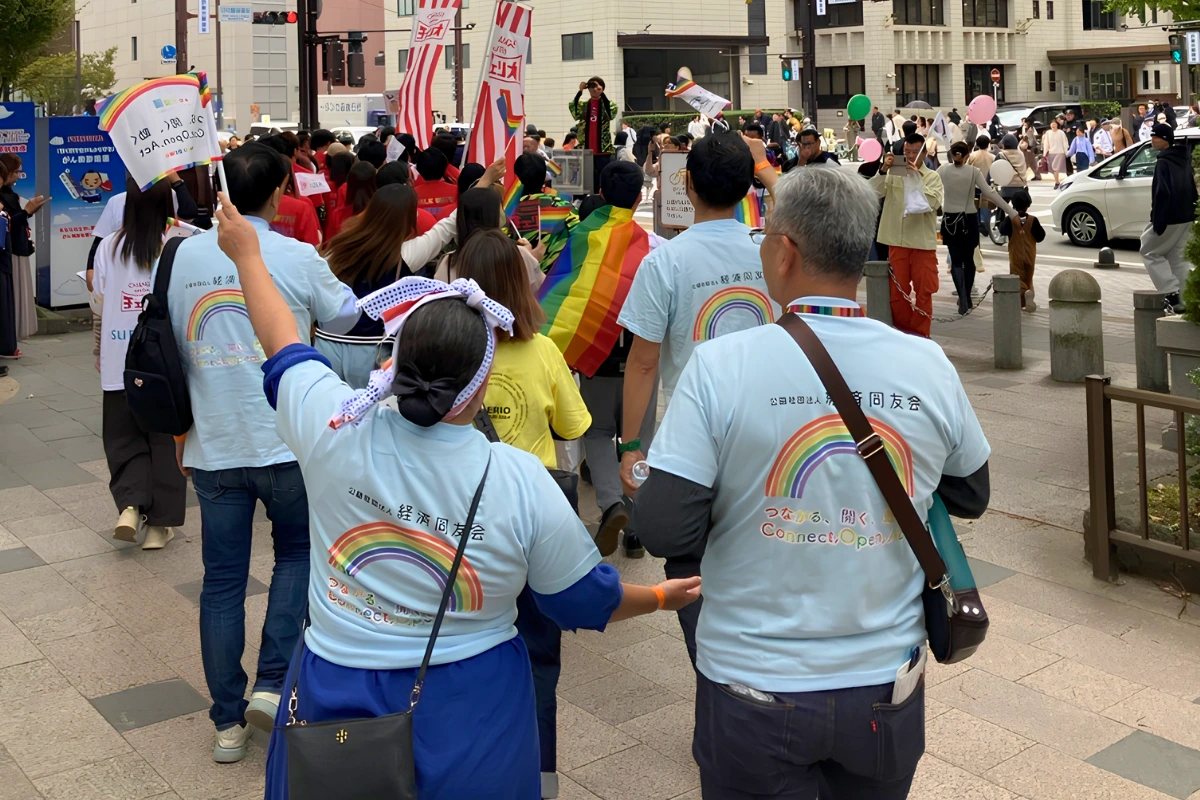 Trans Man Akira Aramaki Makes History Running for Mayor of Fukuoka 12 Participants march in a Pride parade through central Fukuoka, carrying rainbow flags and wearing shirts with rainbow graphics as crowds move along the city street.