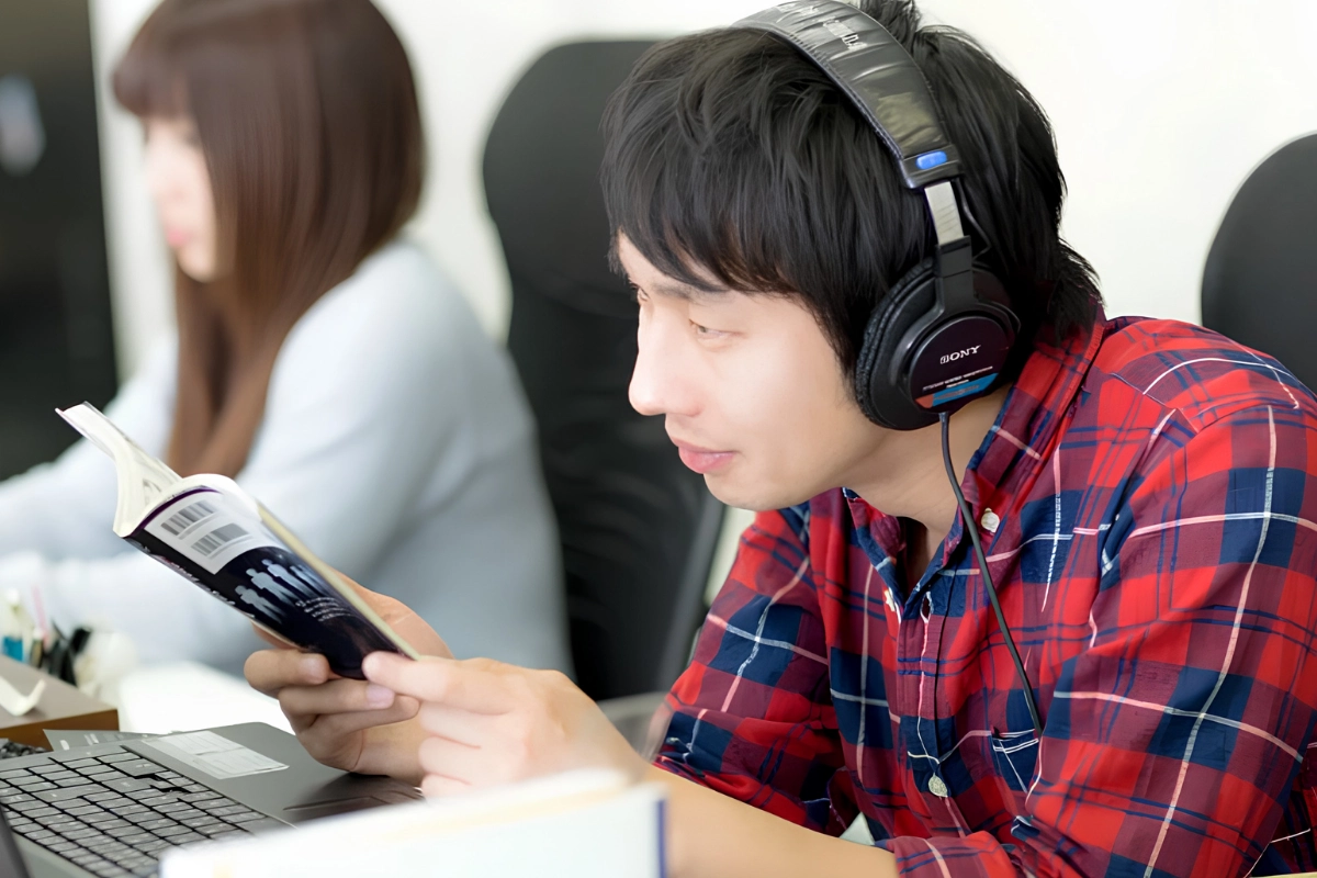 Man is taking a break from work and reading manga and listening to music while sat at his desk.