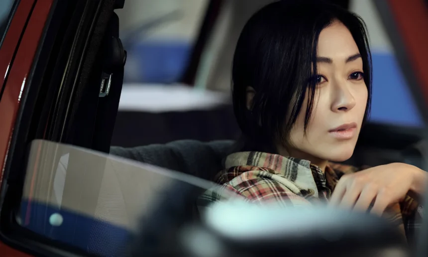 Hikaru Utada is sat in a car with the window down staring ahead with their hand raised near their face