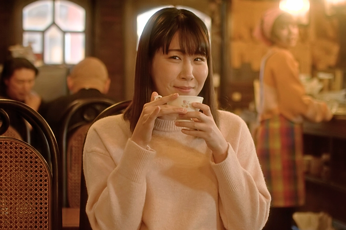 What Makes a Film Queer? Shoji Tsuyoshi on The Trans Girl Next Door and LGBTQ+ Cinema 2 Japanese woman with straight dark hair smiles while holding a teacup in a warmly lit café.
