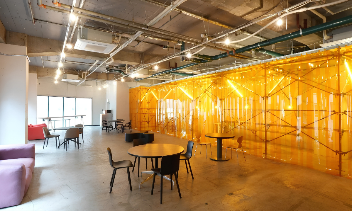 Leave the ROOM: Inside THEA's Queer-Inclusive Art Exhibition in Shinjuku 9 Interior of the WPÜ Shinjuku Gallery. Tables and chairs are sat at the center, while in the background and on the right large translucent plastic strips cover a developing exhibit