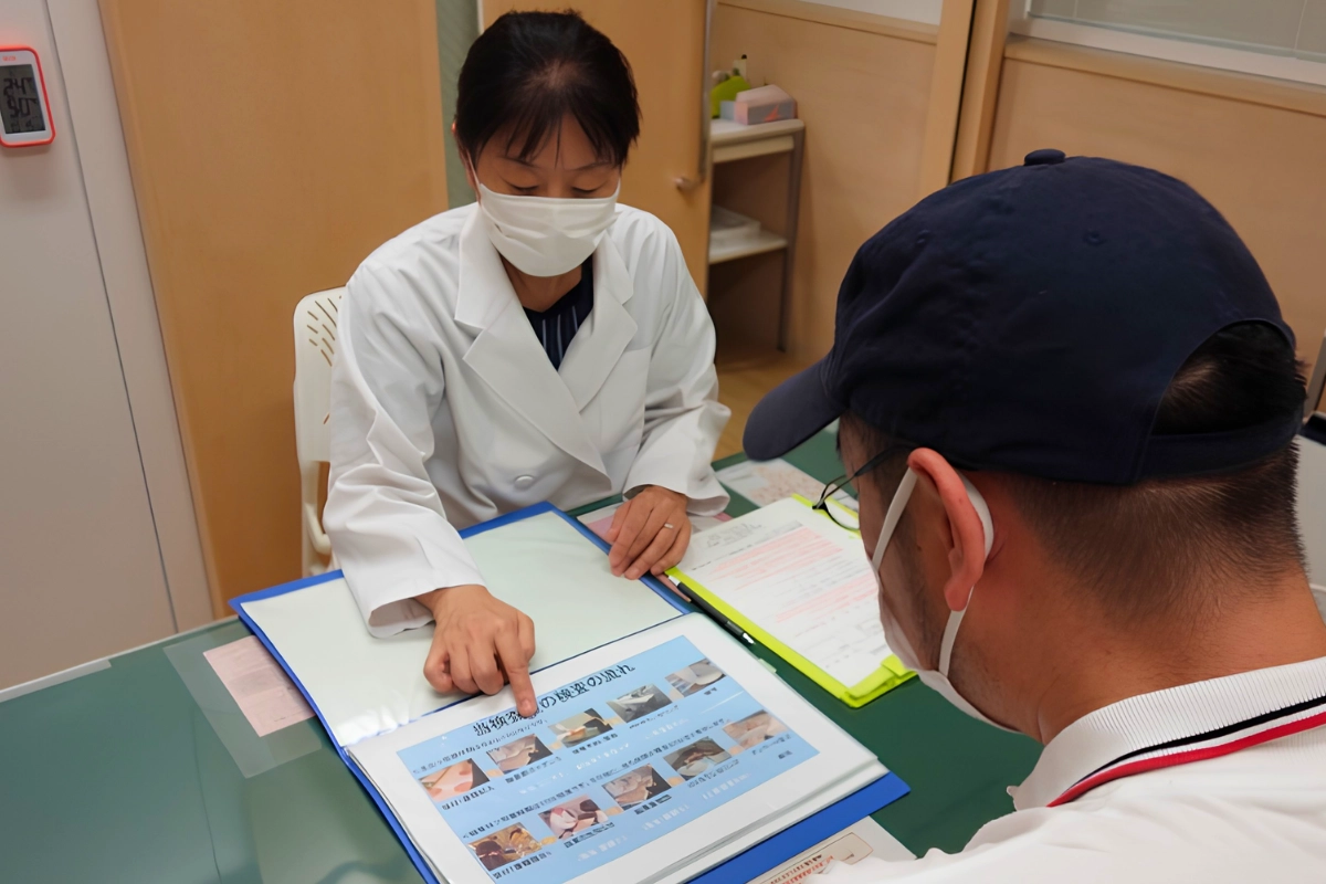PrEP in Japan: How to Get It, Costs, Tests & English-Speaking Clinics 14 Healthcare professional in a Japanese clinic points to testing information while explaining the process to a masked patient seated across the desk.