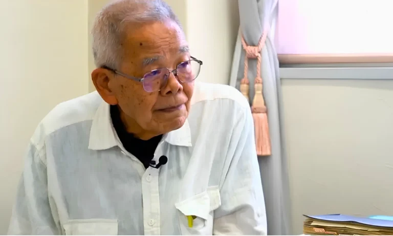 Dr Masayoshi Negishi, wearing glasses sits for an interview with a microphone clipped to his shirt.