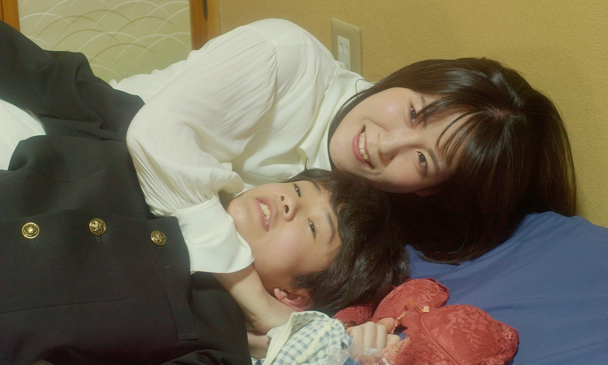 Woman lies beside a younger person indoors, smiling as they rest closely together.