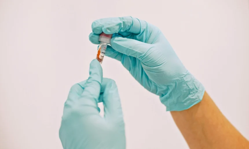 Healthcare worker wearing gloves handles a medical sample in a test tube.