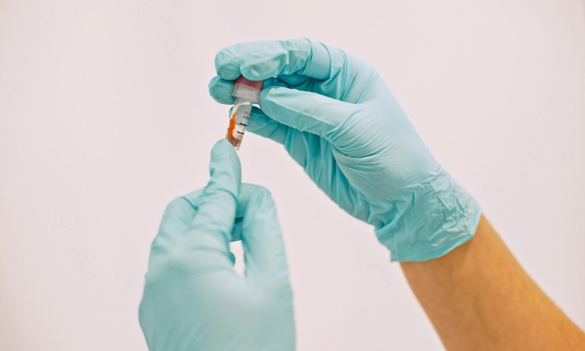 Healthcare worker wearing gloves handles a medical sample in a test tube.