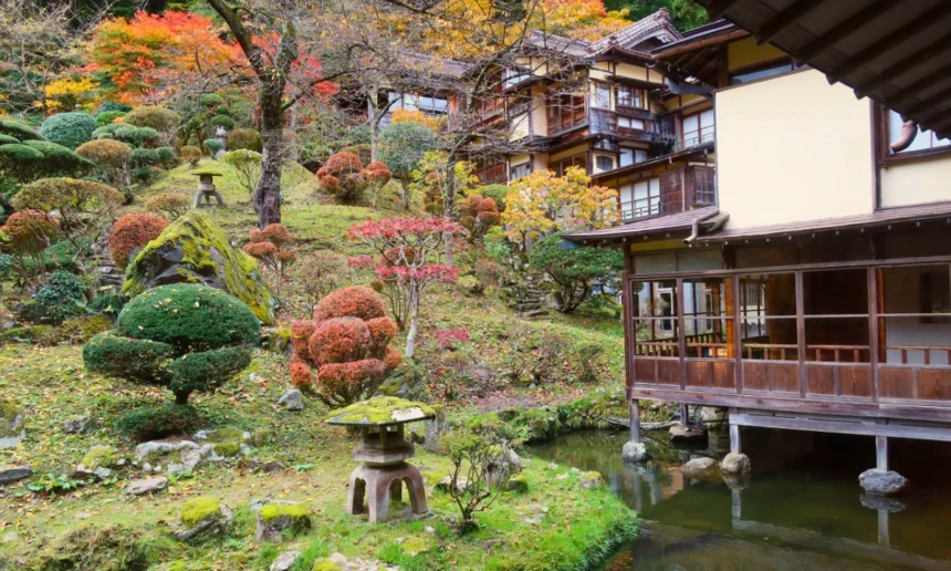 Traditional Japanese ryokan buildings overlooking a landscaped garden with autumn foliage and stone lanterns.
