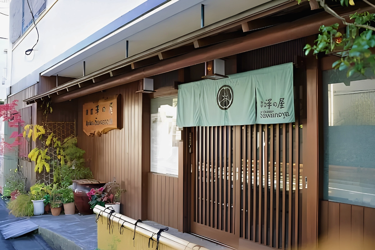 Gay-Friendly Ryokan in Japan: Evidence-Backed Stays for LGBTQ+ Travelers 13 Entrance to Sawanoya Ryokan with wooden lattice doors, a fabric noren curtain, and potted plants.