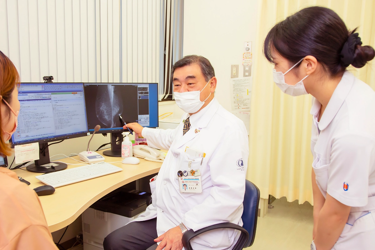 How Breast Cancer Screening Works in Japan for LGBTQ+ People 14 A doctor discusses a mammogram displayed on a computer screen with a patient and nurse.