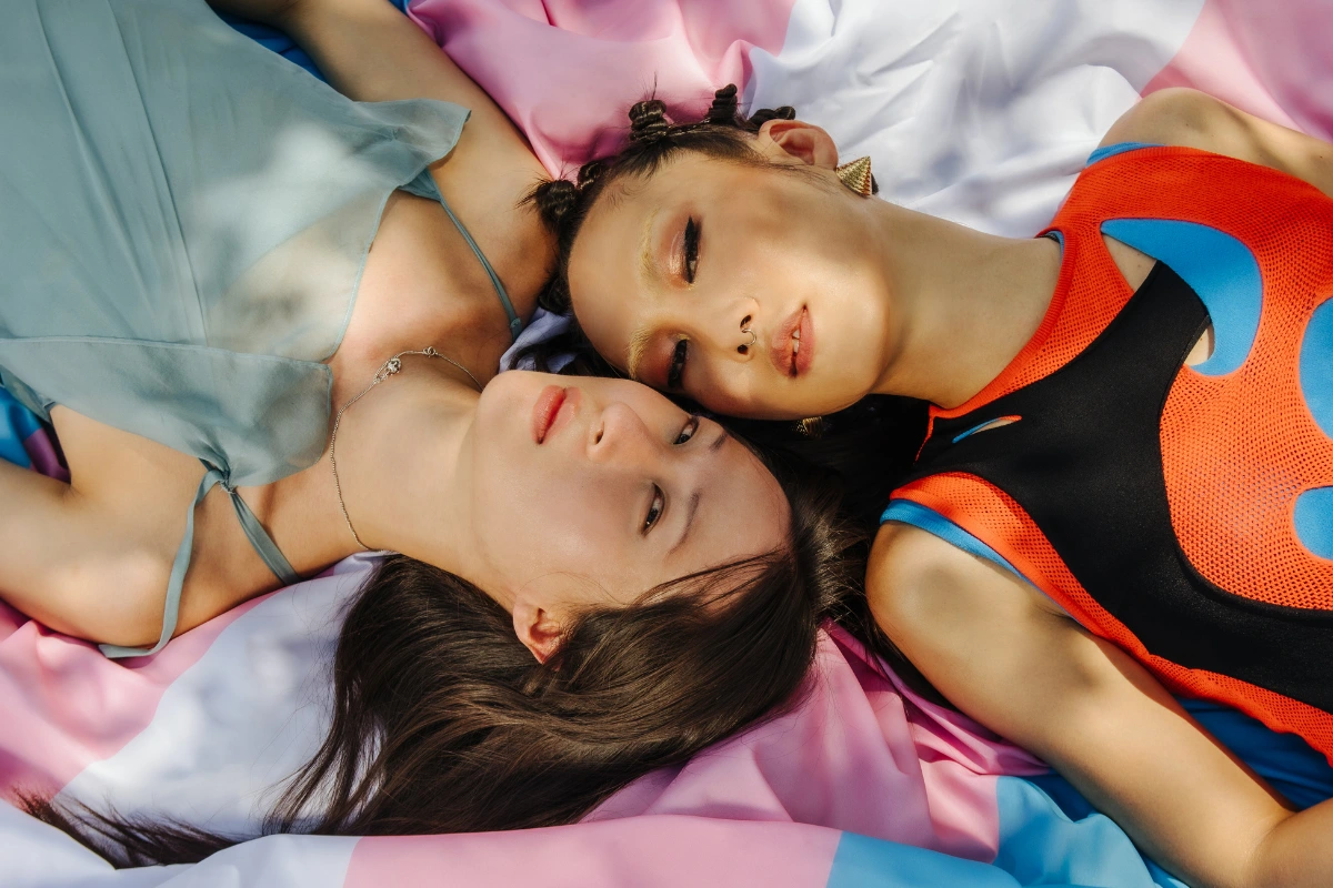 Two asian transgender women led on a transgender pride flag, staring into the camera. 